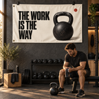The Work Is the Way Banner above an adult athlete resting with a kettlebell in a warm home gym; illustrative lifestyle mockup. Banner has two grommets along the left short edge. Display clips, exercise equipment and room props not included.